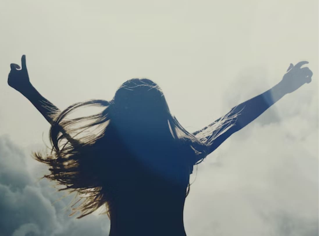 back of woman holding hands up in the sky