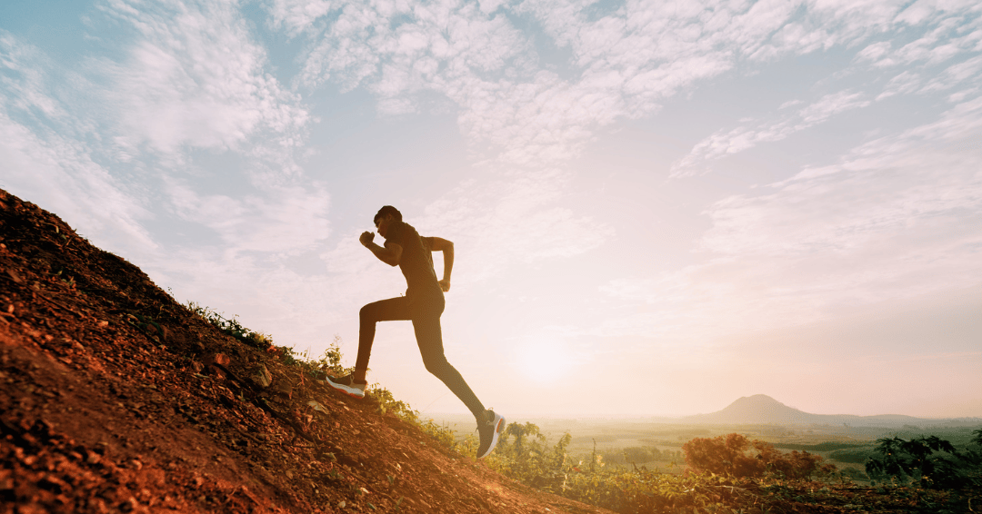 man running up hill with sunset in the background