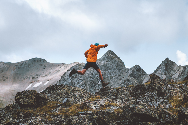 man in orange coat running up mountain