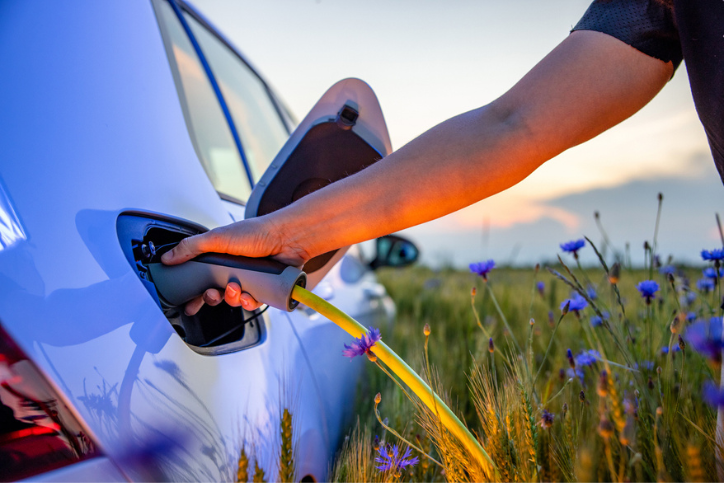 Electric vehicle by meadow field being recharged