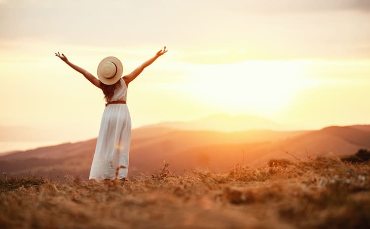 woman in field holding her hands up in the sunset