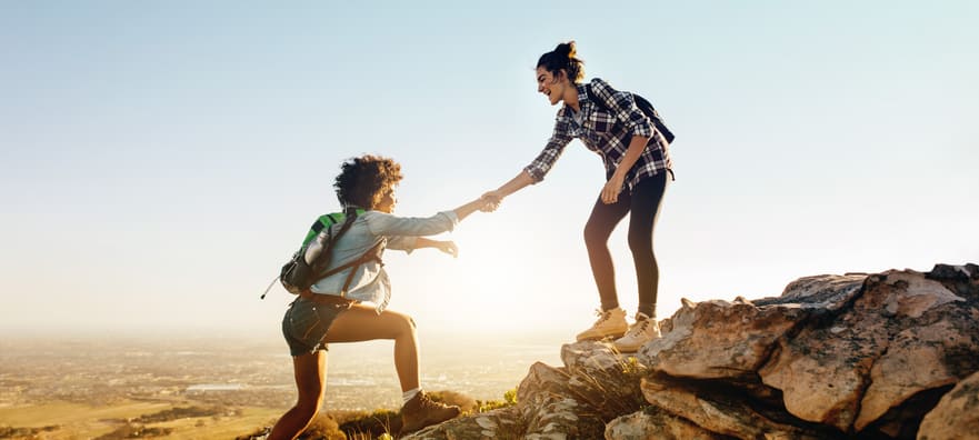 one woman helping another woman onto the side of a cliff