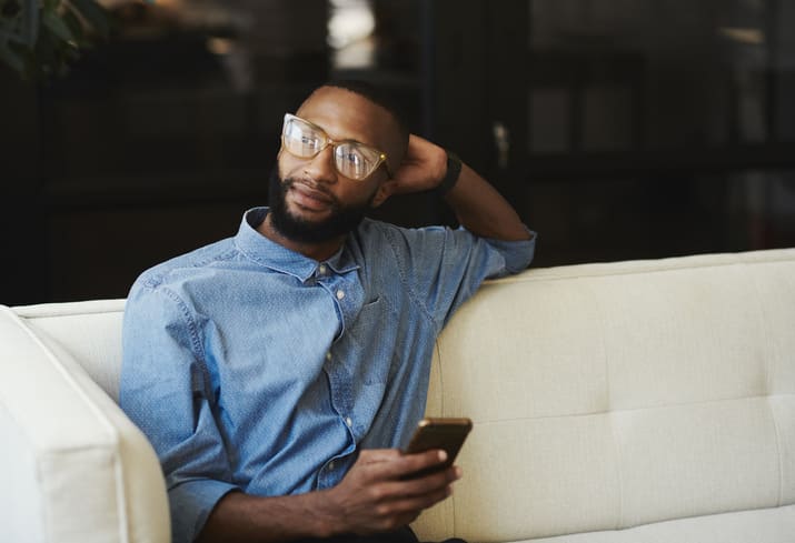 man sat on sofa looking away from his phone